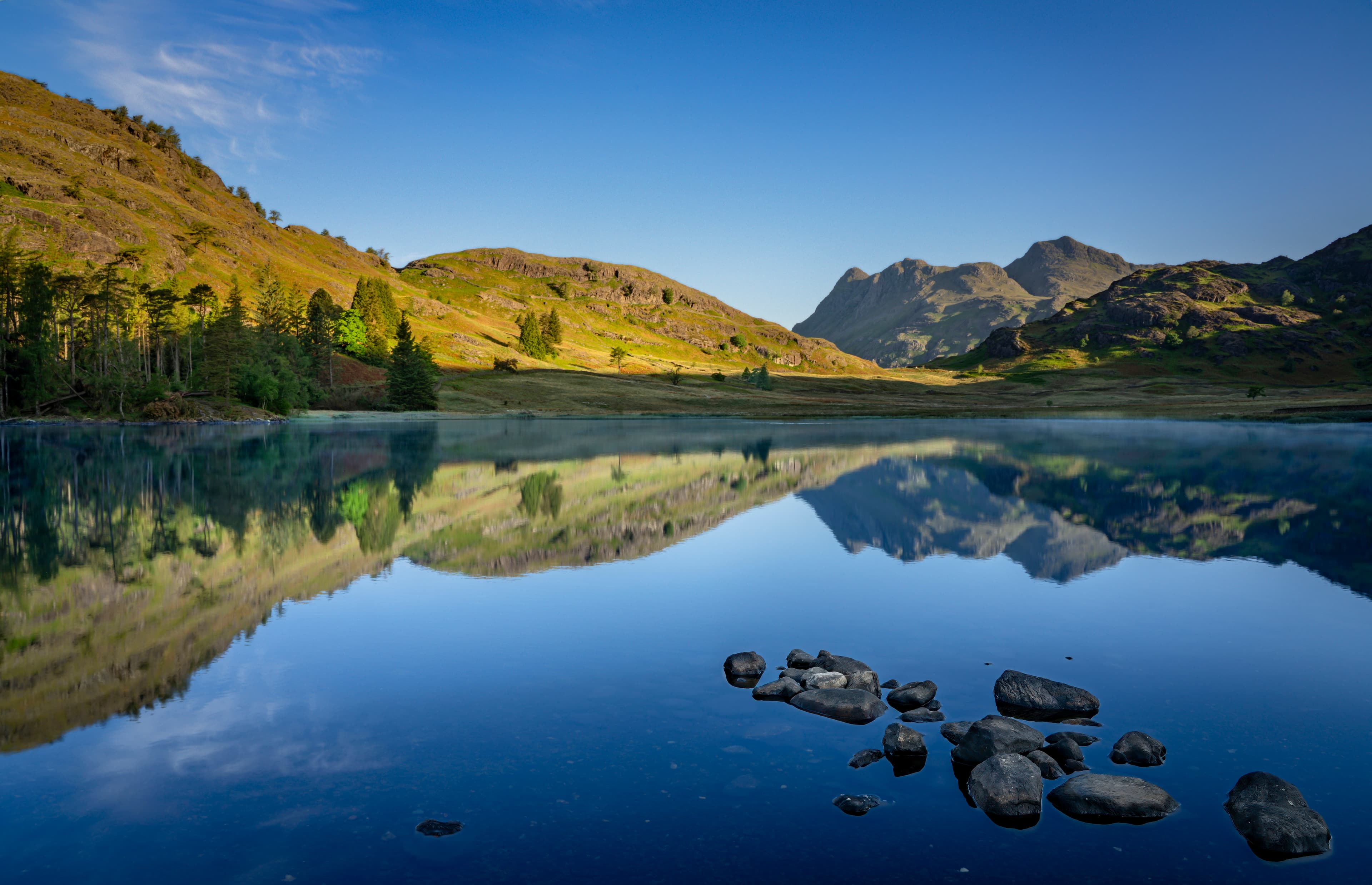 Calm lake reflecting mountains and hills under a blue sky