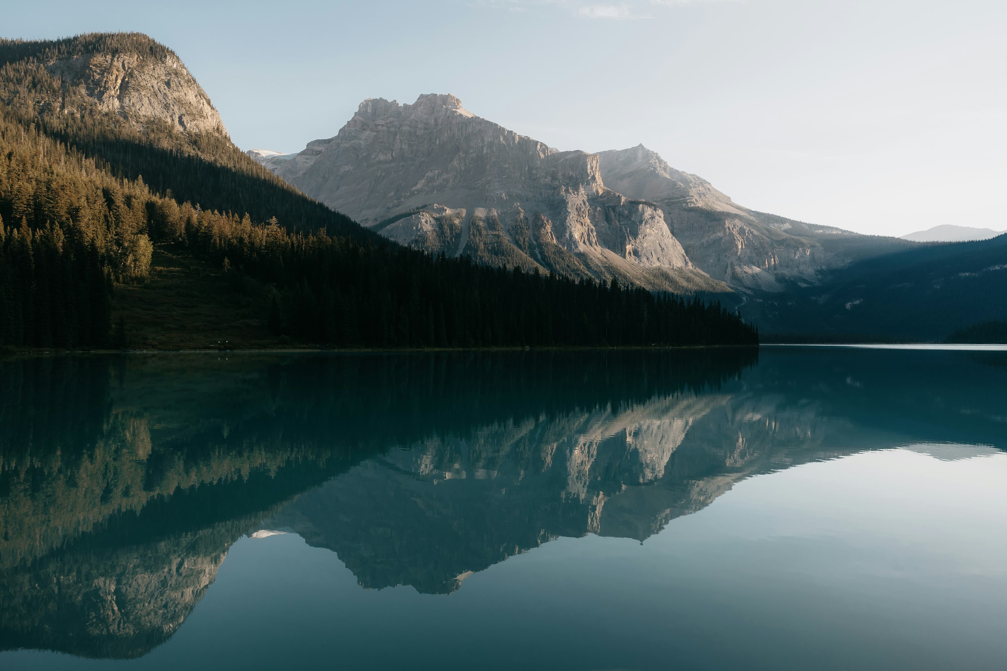 Calm lake reflecting mountains and trees at sunrise, Banff, Canada